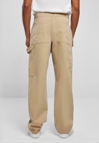 Beige cargobroek met een losse pasvorm, voorzien van twee achterzakken en één zijzak. Gemaakt van katoen met een gladde textuur.
