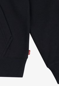 Sweatshirt azul escuro com punhos e bainha canelados, apresentando um bolso lateral e um pequeno rótulo vermelho da Levi's costurado na costura.