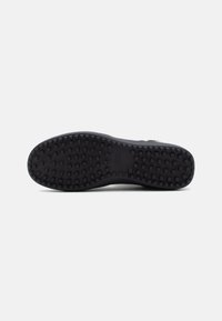 Sole di scarpa sportiva nera con una superficie in gomma testurizzata e a motivo, caratterizzata da piccoli quadrati alti per la trazione. Design piatto con una leggera curvatura.