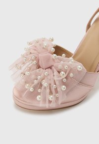 Pink satin slingback shoe with large tulle bow, adorned with white pearls, rounded toe, and smooth texture.