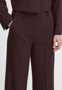 Dark burgundy tailored trousers made of smooth fabric, featuring a flat front, side pockets, and belt loops.