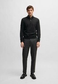 Black zip-up sweater with a high collar, paired with dark gray tailored trousers and black lace-up shoes. Smooth fabric and slim fit.