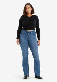 Zwart pluche cropped sweater, hoge blauwe denim jeans met een rechte pijp, lichte waskleur en subtiele stiksels op de zakken. Zwarte enkellaarzen.