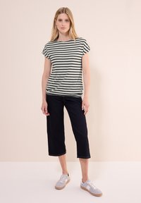 Haut en tricot rayé noir et crème, avec des manches courtes, associé à un jean court foncé et des baskets grises avec des semelles en caoutchouc.