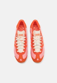 Tenisky Adidas s kombinací růžových a oranžových syntetických a semišových materiálů, s bílými tkaničkami a třemi oranžovými pruhy po stranách.