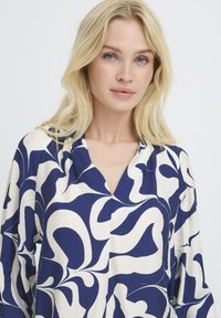 Marineblaue und cremefarbene Bluse mit Muster, V-Ausschnitt, langen Ärmeln und einem fließenden, leichten Stoff mit abstrakten wirbelnden Designs.