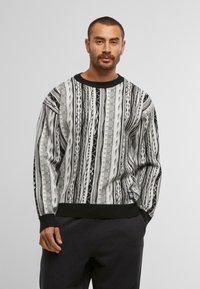 Gestrickter Pullover in Schwarz, Grau und Weiß mit einem vertikalen Muster. Verfügt über einen gerippten schwarzen Halsausschnitt und Ärmelbündchen. Weicher Stoff.