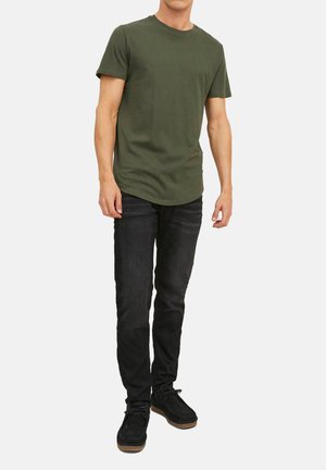 Olive green short-sleeve cotton t-shirt with a round neckline, paired with dark denim jeans and black shoes with a textured finish.
