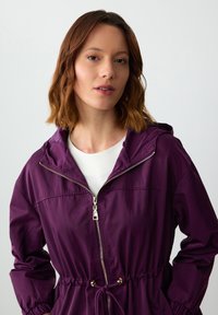 Paarse capuchonjack van lichtgewicht materiaal, met een rits aan de voorkant, een verstelbare taille en elastische manchetten voor een getailleerde look.