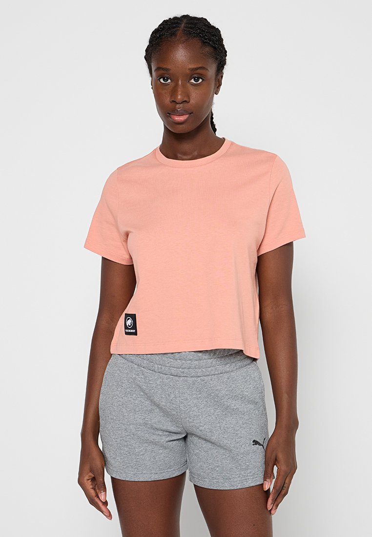 Różowa, krótka koszulka z krótkim rękawem z czarną naszywką z logo, w zestawieniu z szarymi szortami sportowymi z czarnym logo. Gładka tekstura.