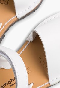 Sandali bianchi in pelle con un design minimalista, caratterizzati da una fascia cucita e una soletta beige. La suola è grigia e texturizzata.