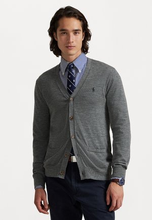Cardigan gris avec un col en V, des boutons en bois et deux poches avant, superposé sur une chemise à rayures bleues et une cravate à motifs.