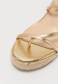 Kuldmetallist espadrille sandaal tekstureeritud jute tallaga, millel on risti rihmad ja varbapadi. Sisetallal on sile heledat tooni vooder.