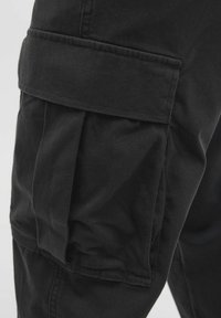 Schwarze Cargo-Hosen mit großzügigen Seitentaschen, einem weichen Baumwollmaterial und einer lässigen Passform. Der Stoff hat eine glatte Textur mit leichtem Glanz.