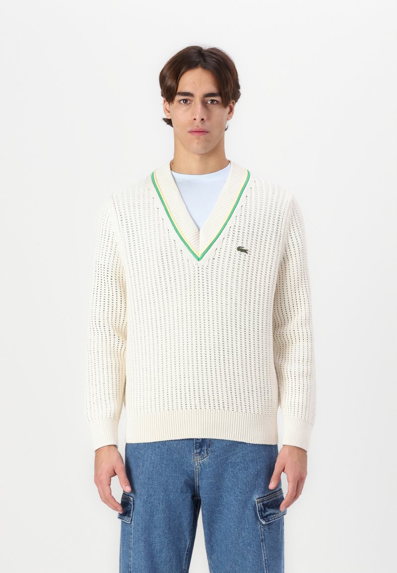 Maglione leggero in crema lavorato a maglia con scollo a V, caratterizzato da dettagli a coste verde e blu navy. Materiale leggero con un motivo a trama aperta.