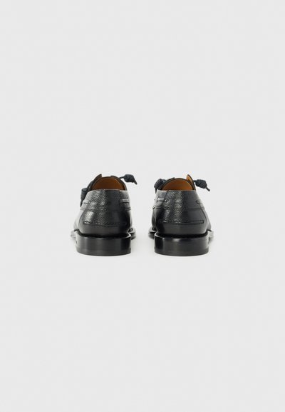 Chaussures en cuir noir avec une finition texturée, orteils arrondis et une fine semelle noire ; présentent un laçage décoratif à l'arrière.