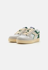Low-top sneakers with a white leather upper, green suede accents, beige laces, and a beige rubber sole. Perforated toe box details.