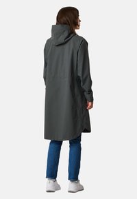 Cappotto lungo impermeabile grigio con cappuccio, tasche laterali e orlo curvo. Abbinato a jeans blu e sneakers bianche.