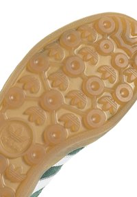 Kengän pohja, joka on valmistettu läpinäkyvästä kumista, jossa on pyöreitä ja lehden muotoisia kuvioita, teksturoitu pinta ja logotiedot.