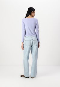 Light purple long-sleeve top, relaxed-fit, paired with light blue wide-leg jeans featuring distressed detail. Stylish animal print shoes.
