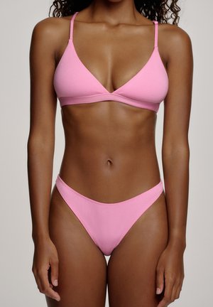 Kvinde iført en pink to-delt bikini med tynde stropper og en V-udskåret top, vist fra nakke til øverste lår mod en ensfarvet baggrund.