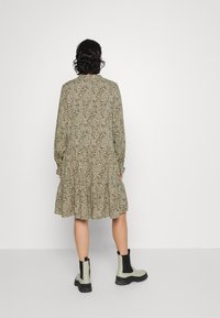 Vestido de comprimento médio com padrão floral em verde-oliva, com mangas longas, bainha com babados e corte relaxado. Combinado com botas de tornozelo pretas e cinzas.