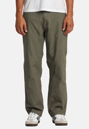 Olive green cotton pants with a relaxed fit, straight legs, front pockets, and visible stitching; worn with white and black athletic shoes.