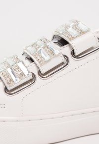 Baskets en cuir blanc dotées de trois brides décoratives ornées d'éléments brillants transparents, d'accents métalliques et d'une semelle en caoutchouc texturée.