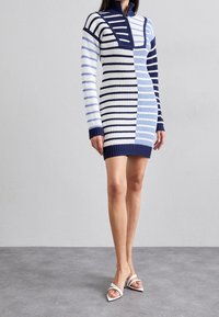 Robe en maille à col montant, présentant des rayures horizontales et verticales en bleu, marine et blanc. Silhouette ajustée, longueur au-dessus du genou.