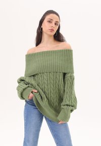 Prevelik, pulover v zeleni barvi z odprtimi rameni in rebrastimi ter kabli pletenimi vzorci. Ima široke manšete in mehak občutek. V kombinaciji z modrimi skinny jeans.
