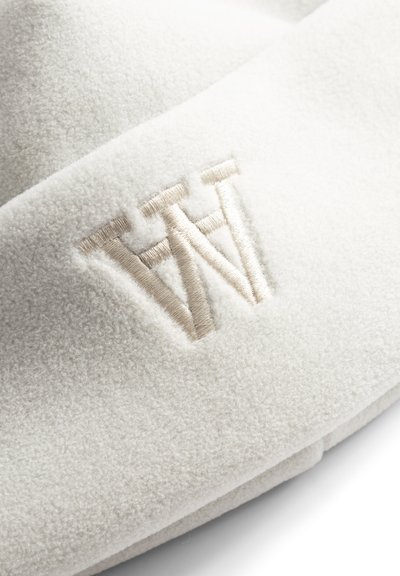 Gros plan sur un tissu polaire blanc avec des lettres brodées en relief beige "WN" cousues à la surface.