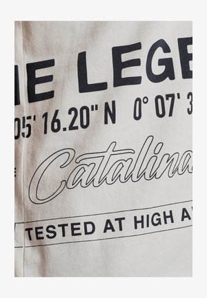 Weißer Stoff mit kräftigem schwarzen Text. Enthält Koordinaten, "Catalina" und "GETESTET IN HOHER HÖHE." Glatte Textur, lässiges Design.