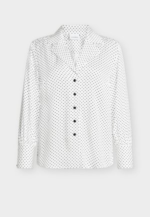 Hvit bluse med lange ermer og svarte prikkete mønster, med hakket krage og knapper foran. Stoffet ser glatt ut med litt glans.