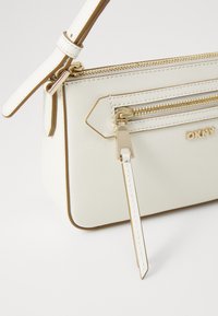 Borsa a tracolla in sintetico bianco con consistenza, dotata di hardware oro, tasca con zip e tracolla regolabile. Logo del marchio visibile.