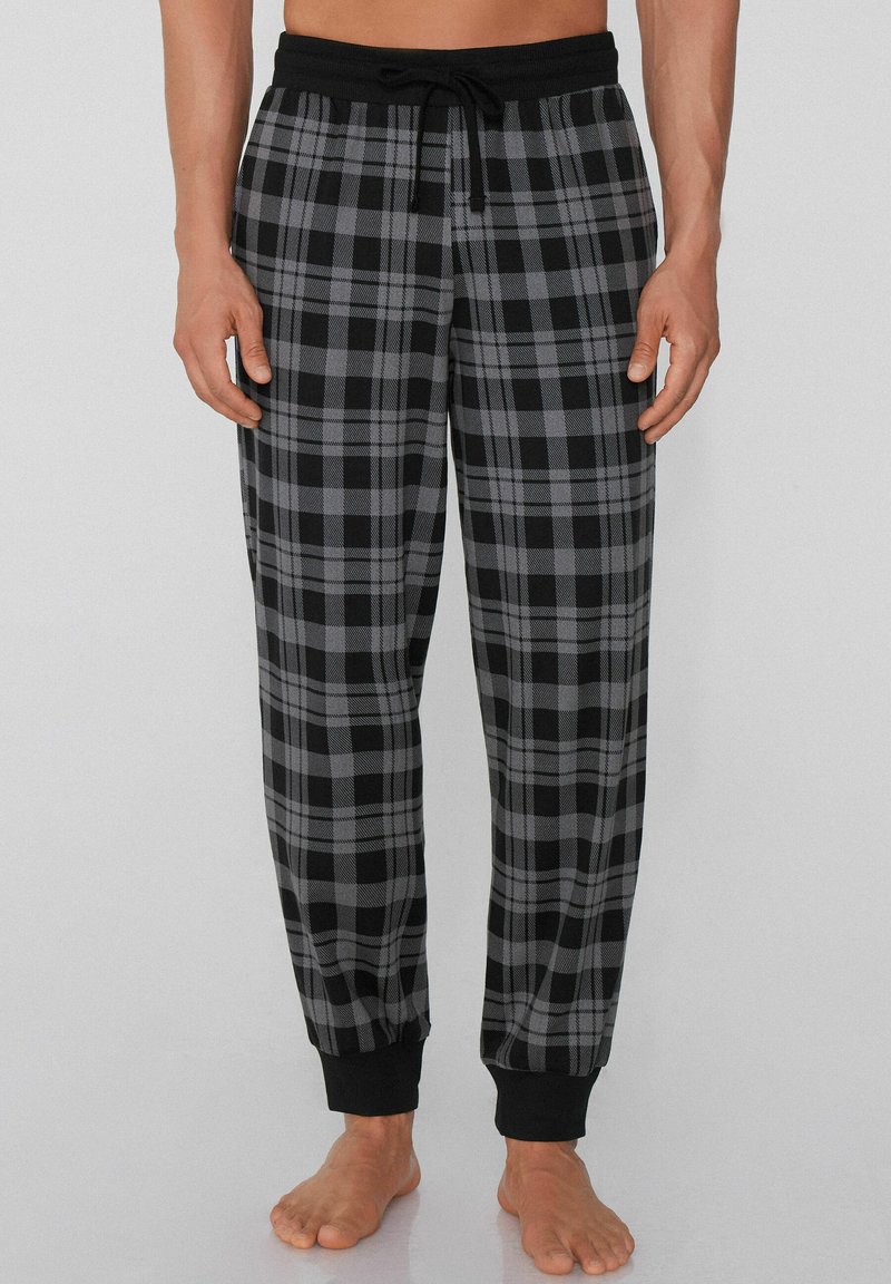 Zwarte en grijze geruite pyjamabroek met een elastische tailleband, trekkoord en elastische boorden bij de enkels. Zacht stoftextuur.