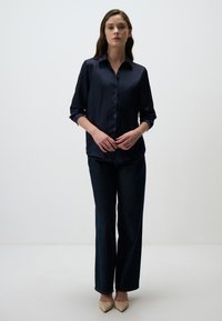 Marineblauwe satijnen overhemd met lange mouwen, gecombineerd met donkere denim wijde broek en beige puntige hakken. Gladde textuur en op maat gemaakt pasvorm.
