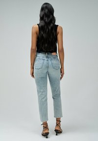 Jeans de tiro alto en azul claro con un corte recto, con bolsillos traseros y dobladillos deshilachados, combinados con tacones negros con tiras.