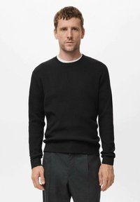 Suéter negro de canalé con cuello redondo y mangas largas, que presenta una tela texturizada y puños ajustados, combinado con pantalones grises.