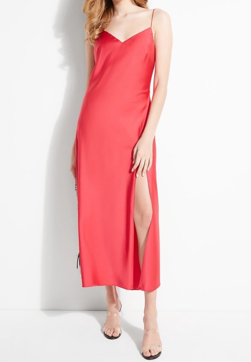 Lang, ærmeløs rød kjole med dyb V-udskæring og sideslids. Glat, satinlignende tekstur. Sammen med gennemsigtige sandaler.