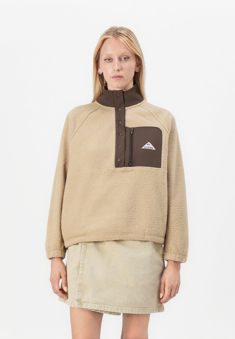 Beige fleece pullover met een brown hoge kraag, kwartrits en een linkse borstzak met een wit logo. Gelaagd, zacht stoffen afwerking.