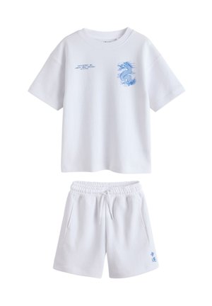 Chemise blanche à manches courtes avec imprimé dragon bleu et short blanc assorti avec texte bleu sur la jambe gauche, tous deux avec une ceinture élastique décontractée.