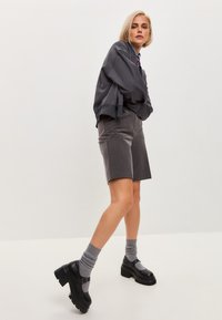 Hanorac oversized gri, purtat peste o cămașă albastră cu guler, asortați cu pantaloni bermuda gri și pantofi masivi negri cu șosete gri.