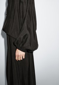 Schwarzes Kleid mit langen, voluminösen Ärmeln, gerafften Bündchen und einer fließenden Silhouette. Die glatte Textur ergänzt das minimalistische Design.