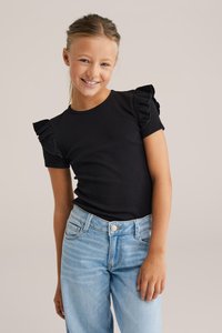 Černý žebrovaný top s krátkým rukávem a volánkovými detaily, v kombinaci se světle modrými džíny v klasickém pětipocketovém stylu.