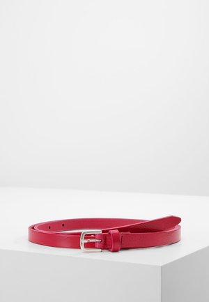 Ohut kapea punainen nahkavyö hopeisella soljella, kierrettynä valkoisella pinnalla yksinkertaista vaaleaa taustaa vasten.