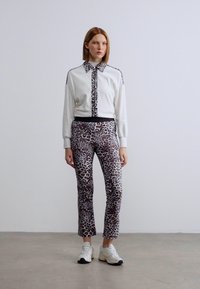 Λευκός φούτερ με λεπτομέρειες σε λεοπάρ σχέδιο, συνδυασμένο με εφαρμοστά παντελόνια με λεοπάρ σχέδιο. Και τα δύο είναι κατασκευασμένα από απαλό ύφασμα. Το υπόδημα είναι λευκά αθλητικά παπούτσια.