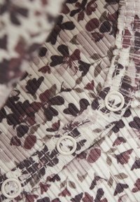 Blommönstrad tyg med ribbat mönster i dämpade vita, lila och mörkrosa nyanser. Har vita knapplås.