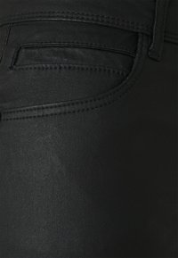 Jeans de mezclilla negra con una textura suave, que cuentan con un bolsillo trasero y detalles de costura sutiles. La tela tiene un ligero brillo.