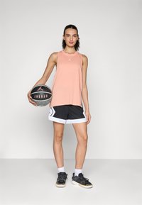 Peach tank top with a logo, black shorts with white trim and patterns, and gray-black basketball shoes holding a basketball.