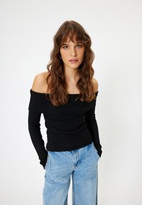 Top nero a spalla scoperta con maniche lunghe a coste, dal design aderente, abbinato a jeans a gamba larga di un blu chiaro. Tessuto morbido, cuciture piatte visibili.
